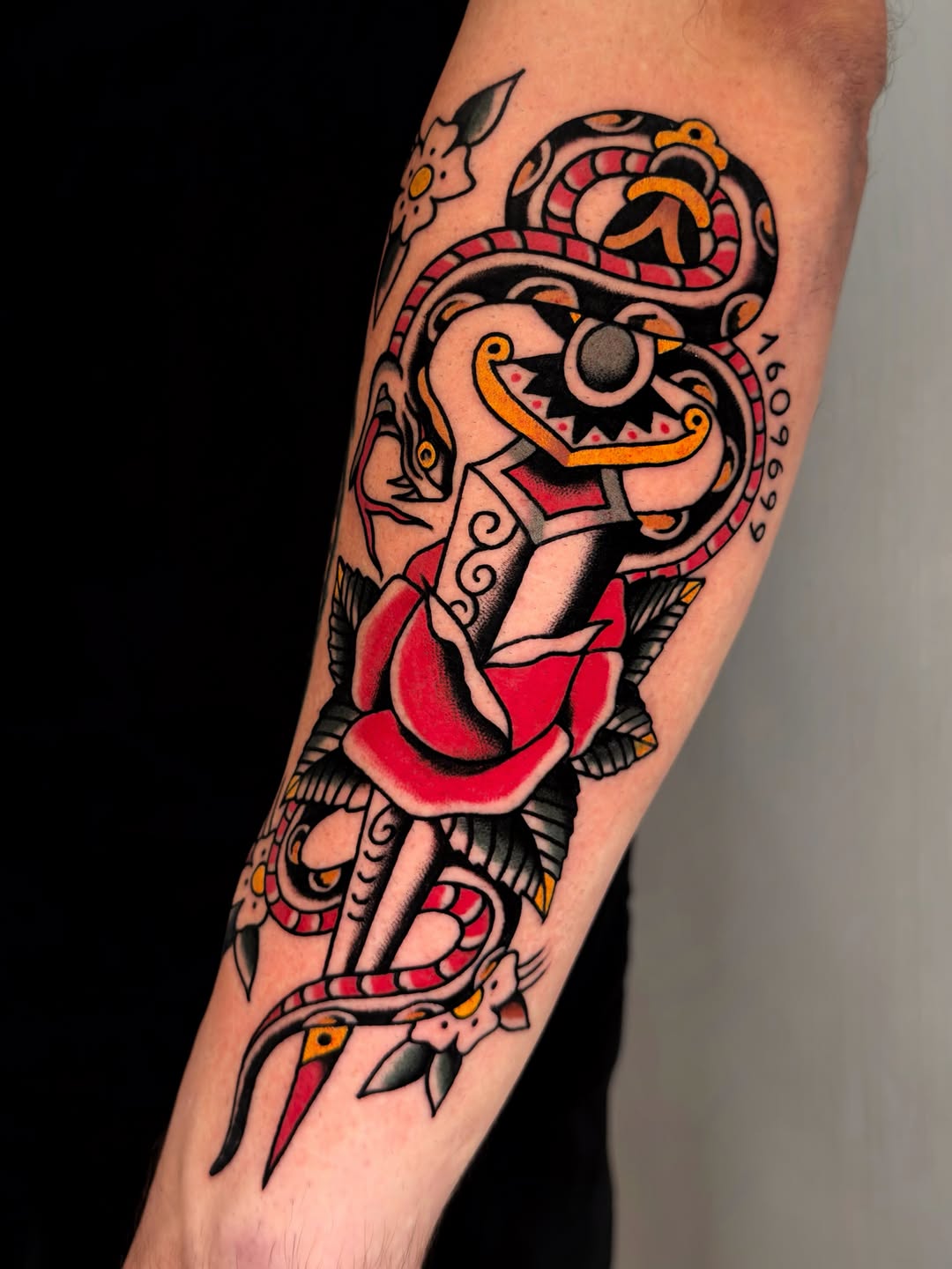 Colorful mask or demon face with red lips and snakes wrapping around the forearm, surrounded by decorative floral elements.