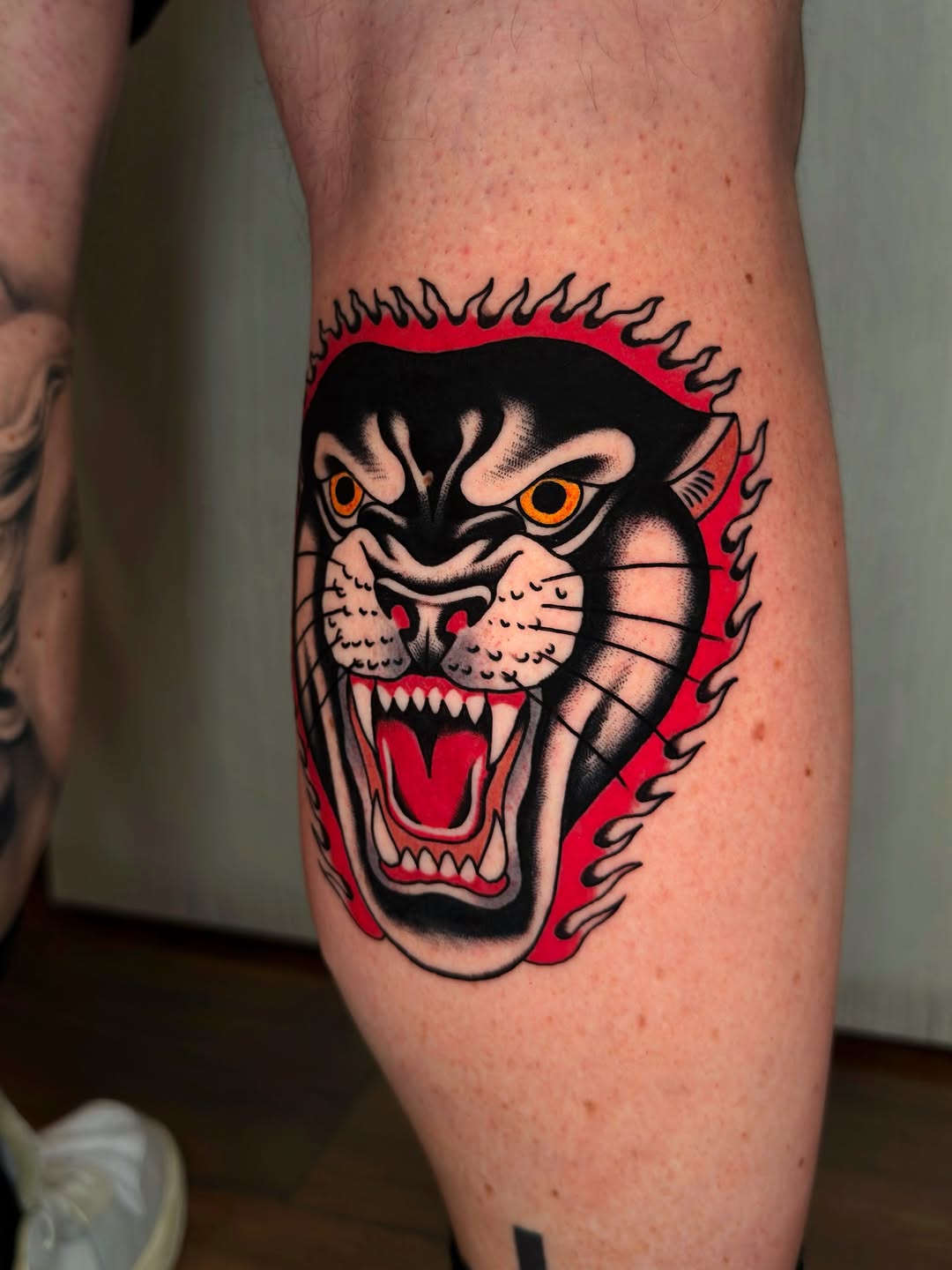 Aggressive panther head with bared fangs, orange eyes, red mane and background, black outlines on calf.