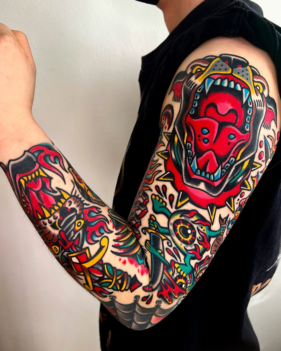 Bold red skull with decorative ornamental flourishes, roses, and traditional flash elements covering both forearms.