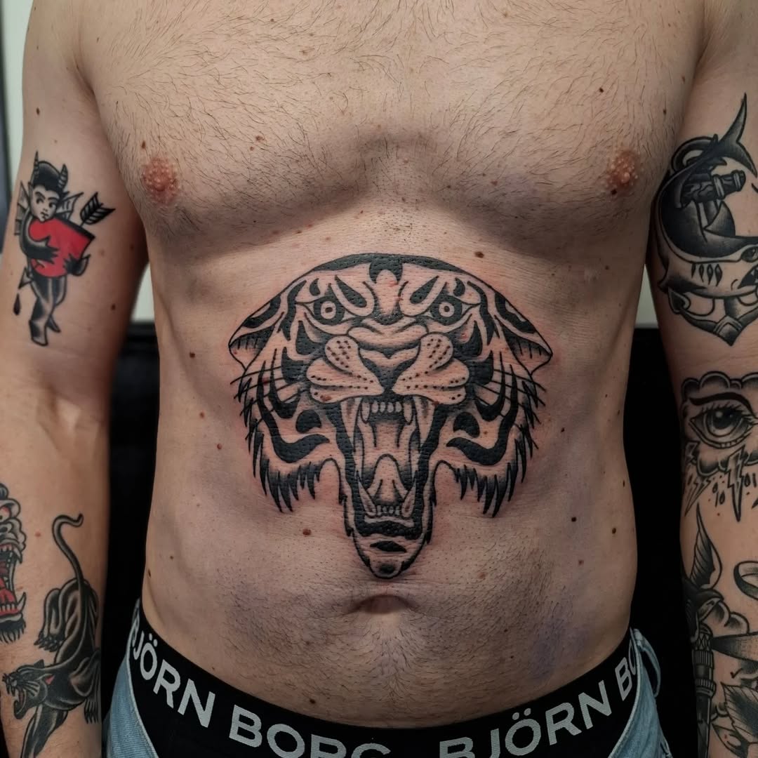 Bold black-outlined tiger head with symmetrical face, gaping mouth, and fierce expression tattooed on chest.