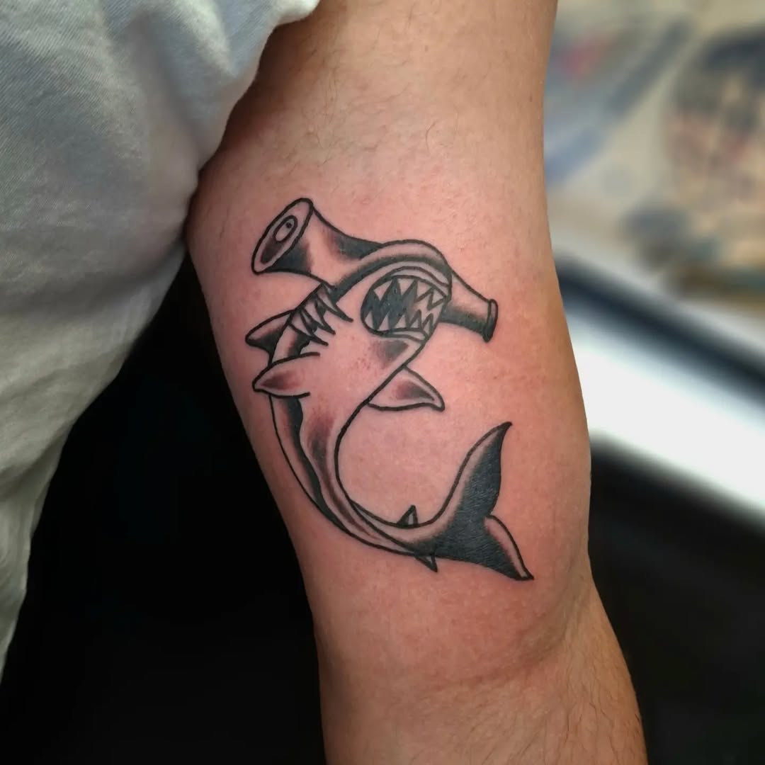 Shark with open mouth holding a megaphone, rendered in bold black outlines on the forearm.