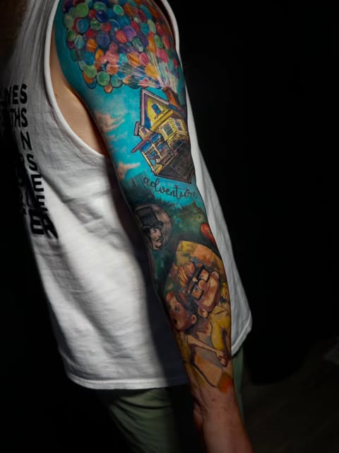 Full-color sleeve tattoo featuring Up house with balloons, Pixar characters, and adventure-themed imagery on upper arm and forearm.