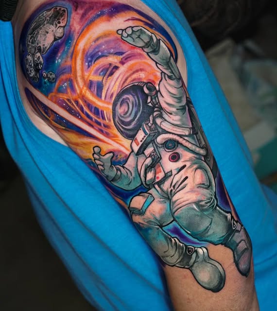 Astronaut in spacesuit reaching toward a colorful cosmic vortex with planets, on upper arm against blue shirt.
