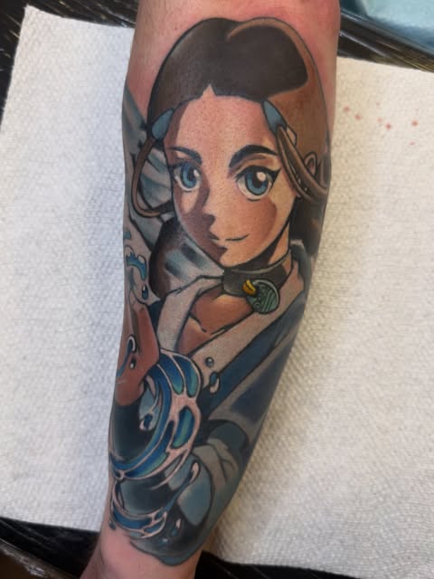 Katara from Avatar: The Last Airbender tattooed on forearm, featuring her face with blue water bending elements and decorative swirls.