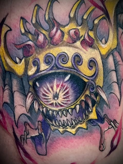 Ornate monster eye tattoo with golden crown, purple teeth, and radiating lashes on pink and purple gradient background on upper arm.