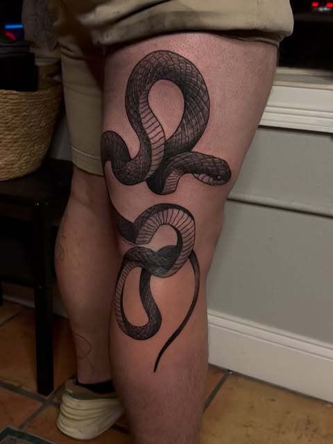 Two intertwined snakes with detailed scale texturing tattooed on the thigh in black and grey ink.