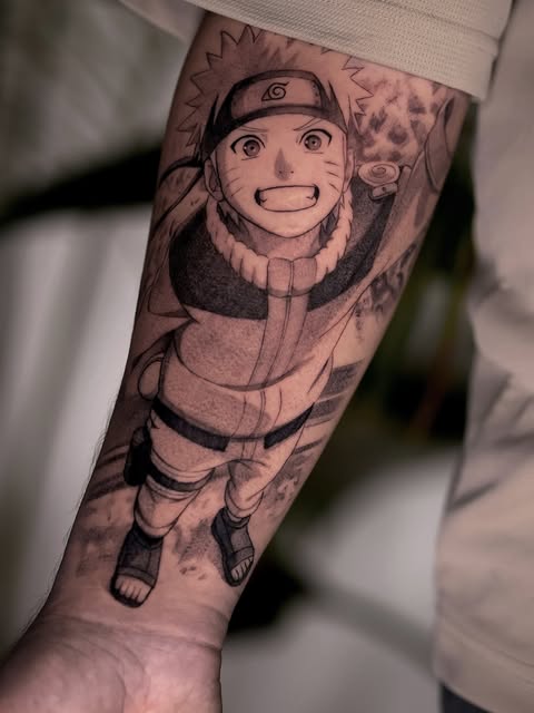 Naruto Uzumaki from Naruto smiling with arms raised, tattooed on forearm in black and grey ink with shading details.