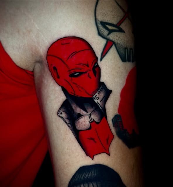Red masked superhero character with black armor plating tattooed on upper arm, featuring detailed facial features and utility belt.