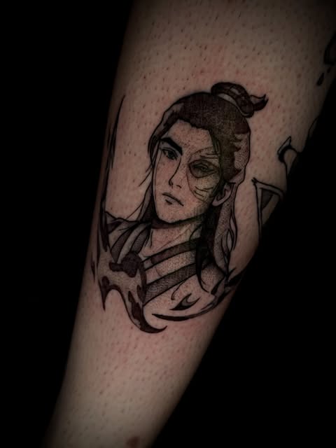 Black and grey portrait tattoo of an androgynous figure with styled hair and facial marks on the forearm, surrounded by flowing ribbon or fabric elements.
