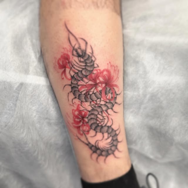 Scorpion tattoo on calf with black segmented body and red flowers interspersed along its length against skin.