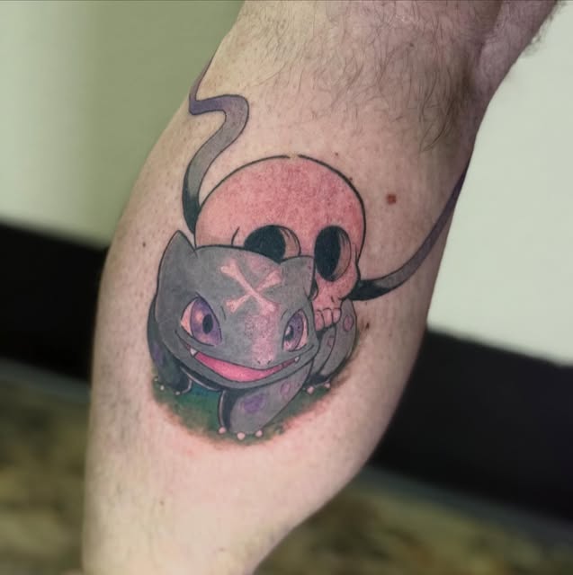 Bulbasaur from Pokémon tattooed on a man's calf, featuring the blue-grey creature with pink mouth and eyes, pink bulb, and green/purple shading around its base.
