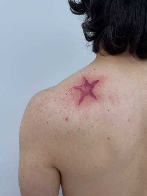 Red star tattoo on upper back shoulder of person with black hair against light background.