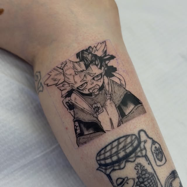 Anime character with spiky hair and serious expression tattooed on forearm in black ink, with additional small decorative tattoos visible below.