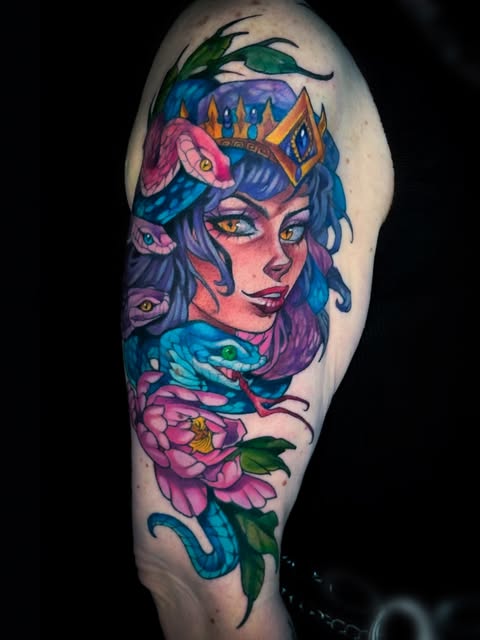 Colorful upper arm tattoo of a mystical woman with purple hair, third eye, crown, surrounded by blue serpents and pink flowers with green leaves.
