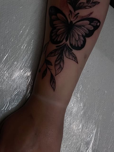 Black and grey butterfly tattoo with detailed wing patterns and flowing leaf designs on the upper arm.
