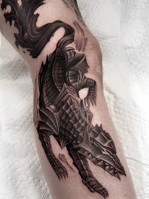 Dragon creature tattoo with scaled wings and detailed linework covering the outer thigh, rendered in black ink.