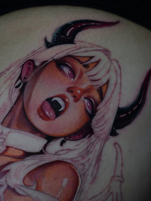 Marilyn Monroe character tattoo on shoulder featuring platinum blonde hair, red lips, and black horns, with pink and flesh tones throughout.