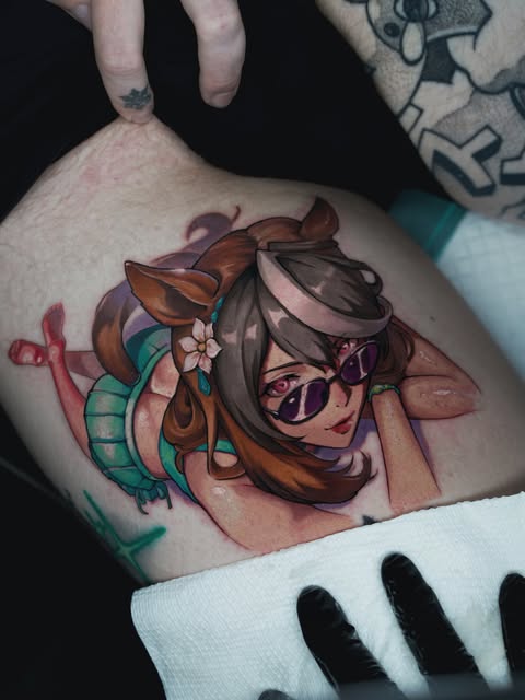 Colorful tattoo on upper arm of a woman with brown hair, sunglasses, and a green snake, featuring teal, orange, and pink tones.
