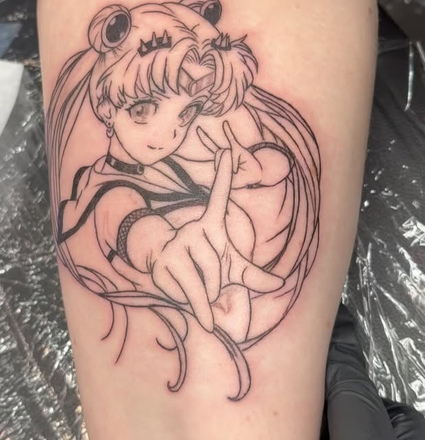 Sailor Moon character with distinctive odango hairstyle and tiara, holding a peace sign, tattooed on upper arm in black outlines.