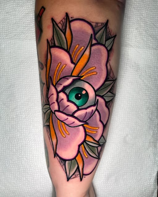 Pink flower with green eye center and orange stamens surrounded by geometric leaf shapes on forearm.