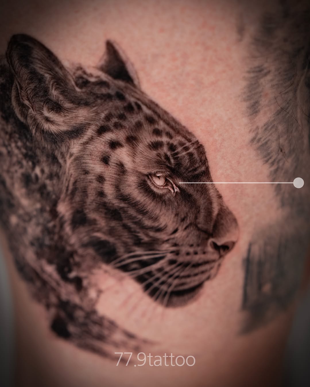 Detailed black and grey leopard head portrait with spotted markings, looking upward on arm or body.