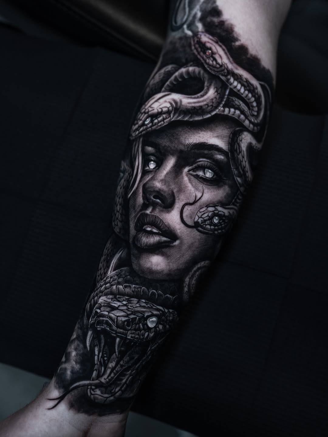 Monochromatic portrait of a woman's face with serpents and reptilian eyes integrated into the composition on the arm.