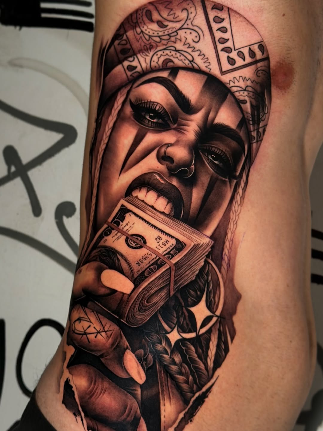 Black and grey portrait tattoo of a woman wearing ornate headwear, holding cash, on upper arm with smooth shading.