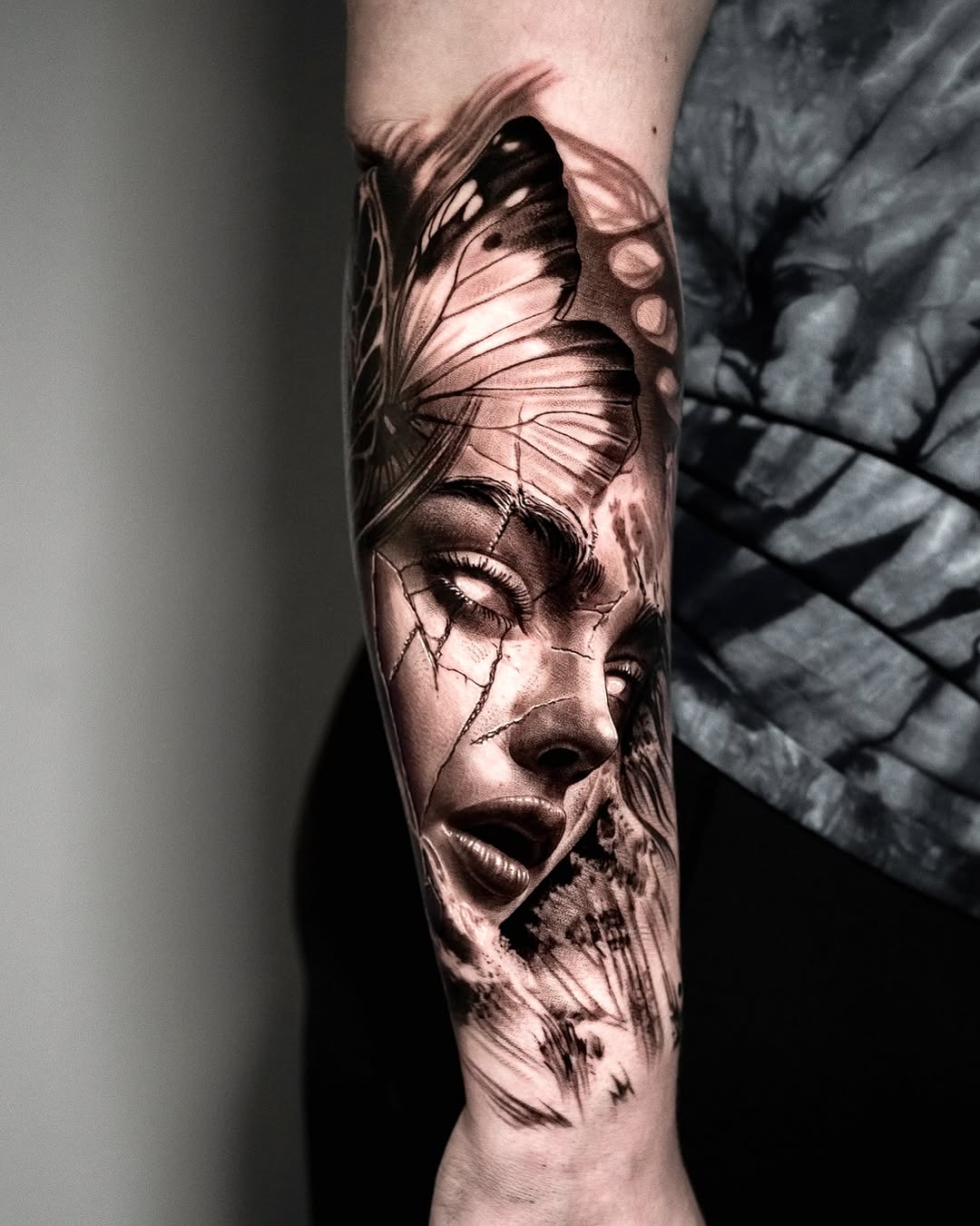 Black and grey portrait tattoo of a woman's face with butterfly wings on forearm, featuring detailed shading and realism.