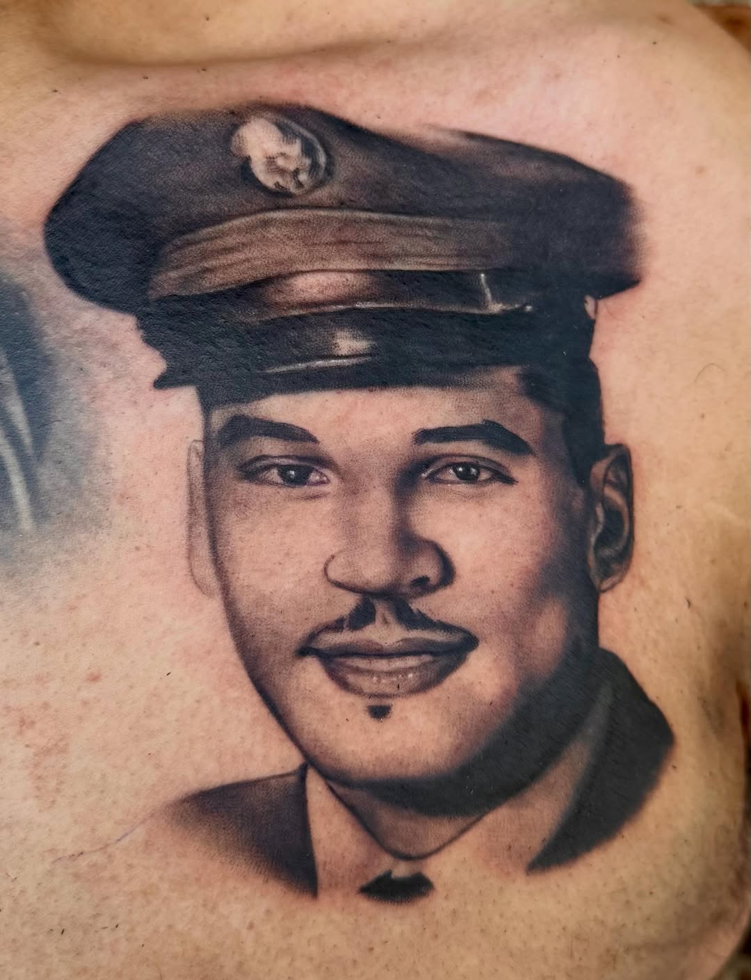 Black and grey portrait tattoo of a man wearing a military cap with insignia, featuring defined facial features and shading on the chest.