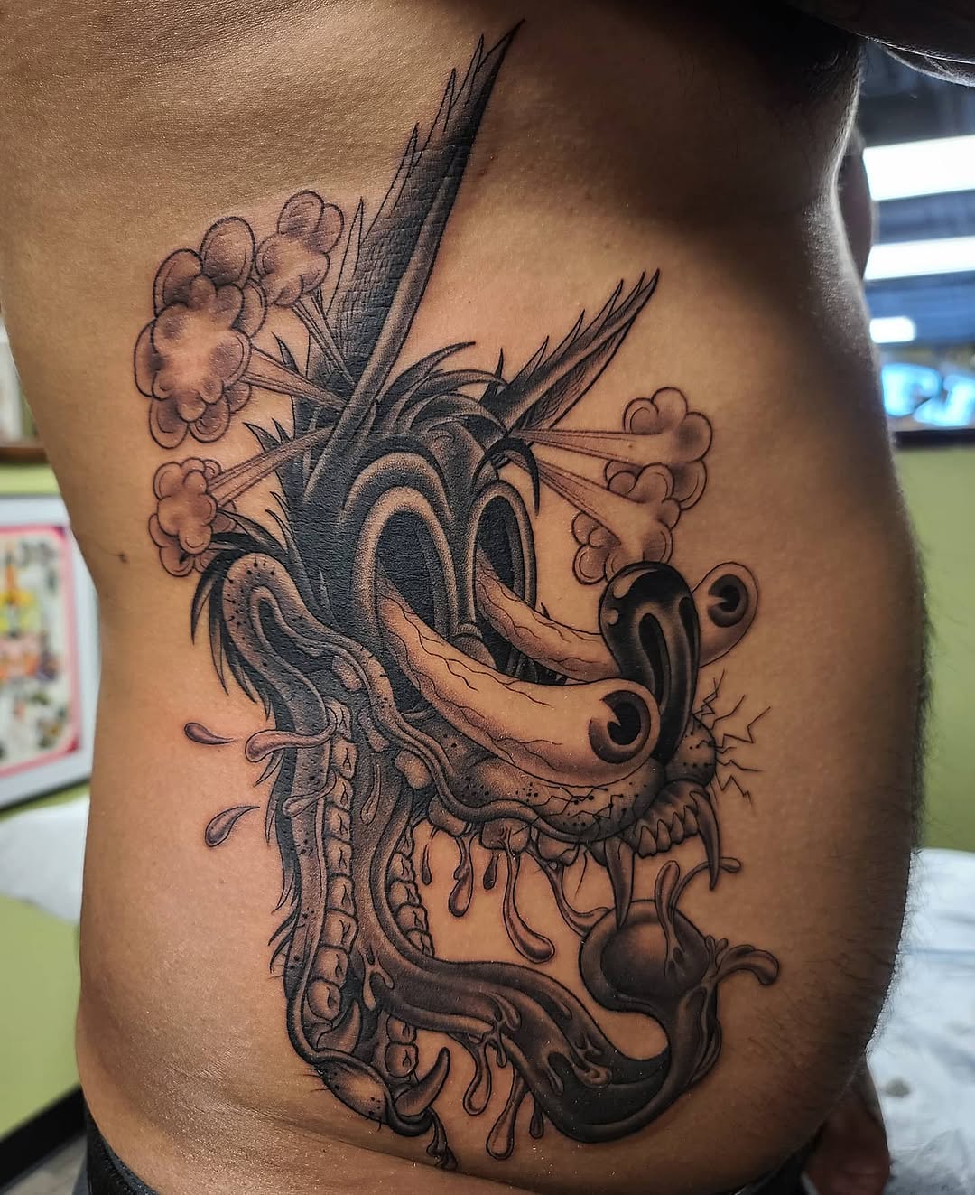 Black and grey dragon head tattoo with ornate details, spiky features, and decorative elements on chest area.