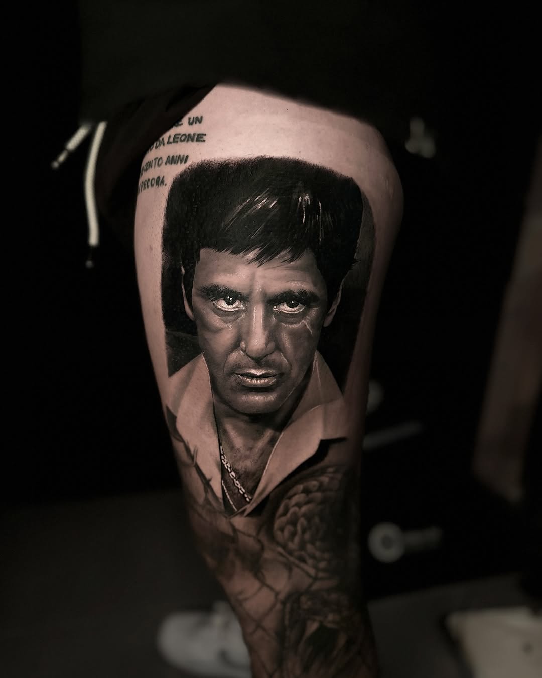 Photorealistic black and grey portrait of a man's face on upper arm, with text visible above the head.