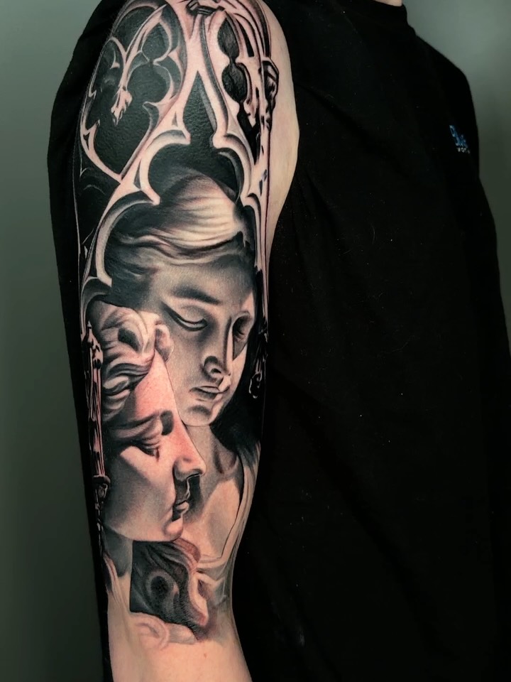 Black and grey portrait tattoo on upper arm featuring multiple overlapping faces with ornate decorative elements above, rendered in realistic shading.