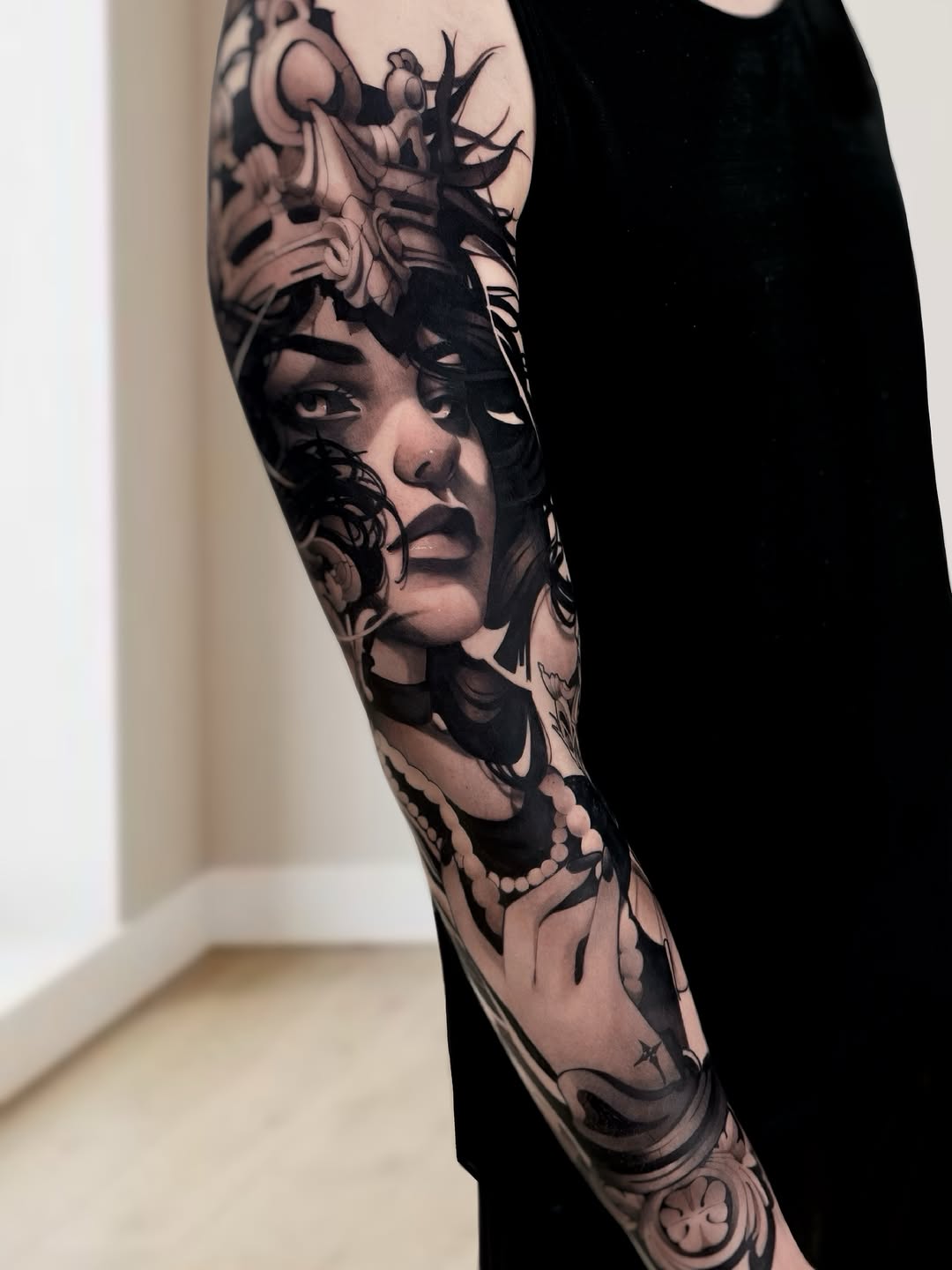 Black and grey portrait sleeve tattoo of a woman's face with ornate decorative elements and baroque designs on the forearm.