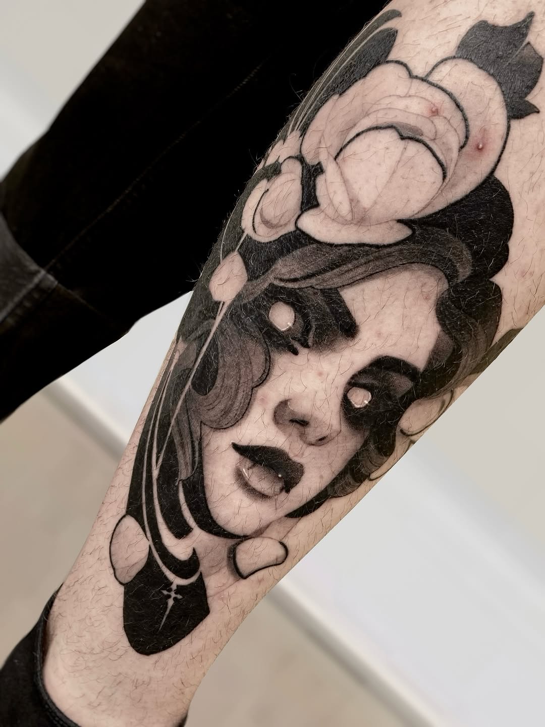 Two stacked portrait faces with expressive features and flowing hair, rendered in black and grey shading on the forearm.