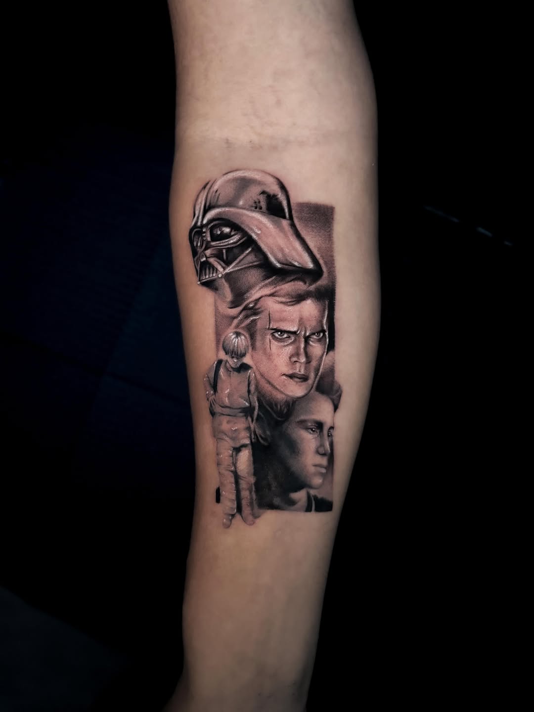 Black and grey portrait tattoo featuring Darth Vader helmet above two male faces on upper arm with realistic shading.