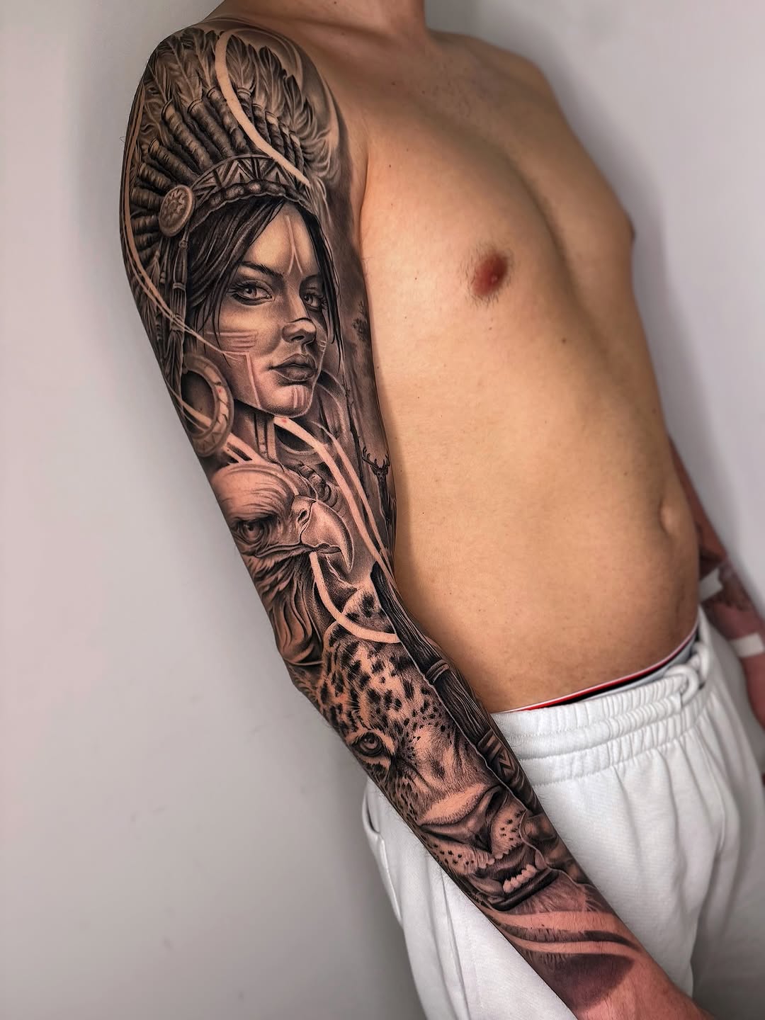 Black and grey full sleeve tattoo featuring a woman with ornate headdress, lion head, and decorative elements on the arm.