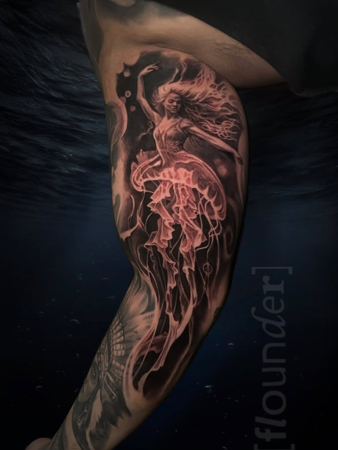 Leg tattoo depicting a woman with flowing hair transforming into a jellyfish, rendered in black and grey with soft shading, on an outdoor sleeve.