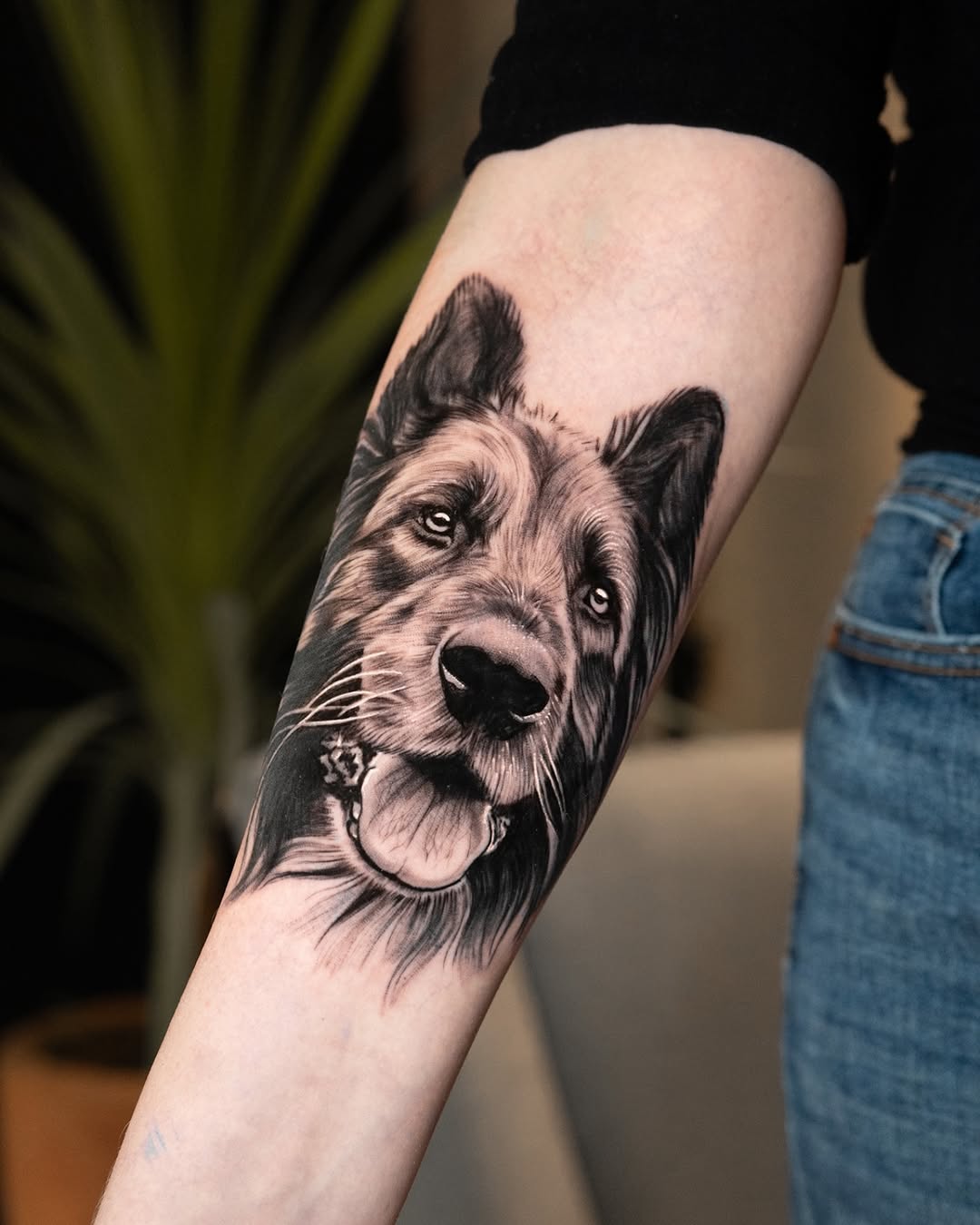 Black and grey portrait of a smiling dog with tongue out, detailed fur texture and expressive eyes on forearm.