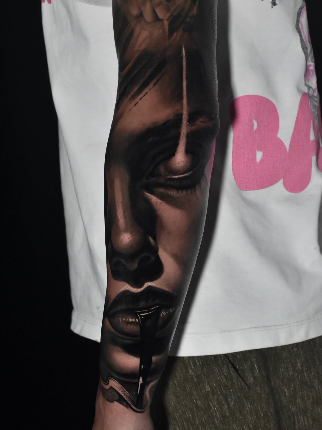 Black and grey realistic tattoo of a woman's face with dripping ink from her lips, on a forearm sleeve.