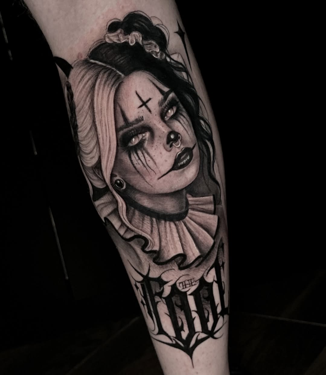 Black and grey portrait tattoo of a woman with dramatic makeup, X marks on forehead, hair bun, and ruffled collar on forearm.