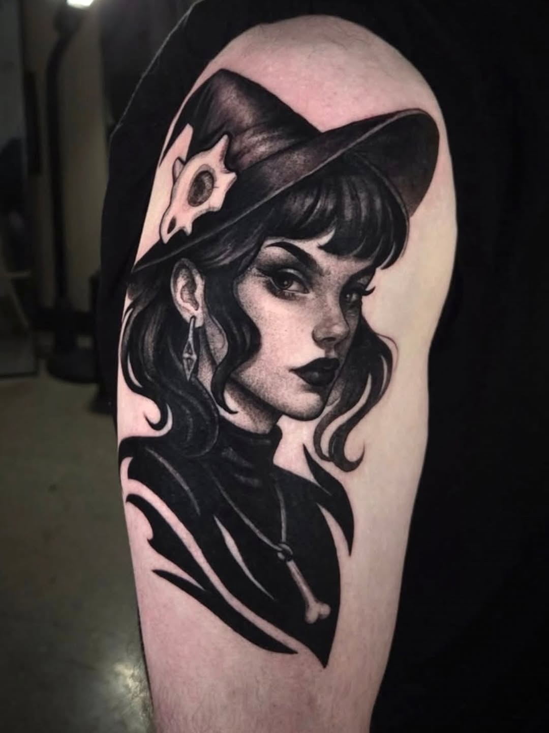 Black and grey portrait tattoo of a woman with wavy hair and fedora hat on upper arm, featuring detailed shading and realism.