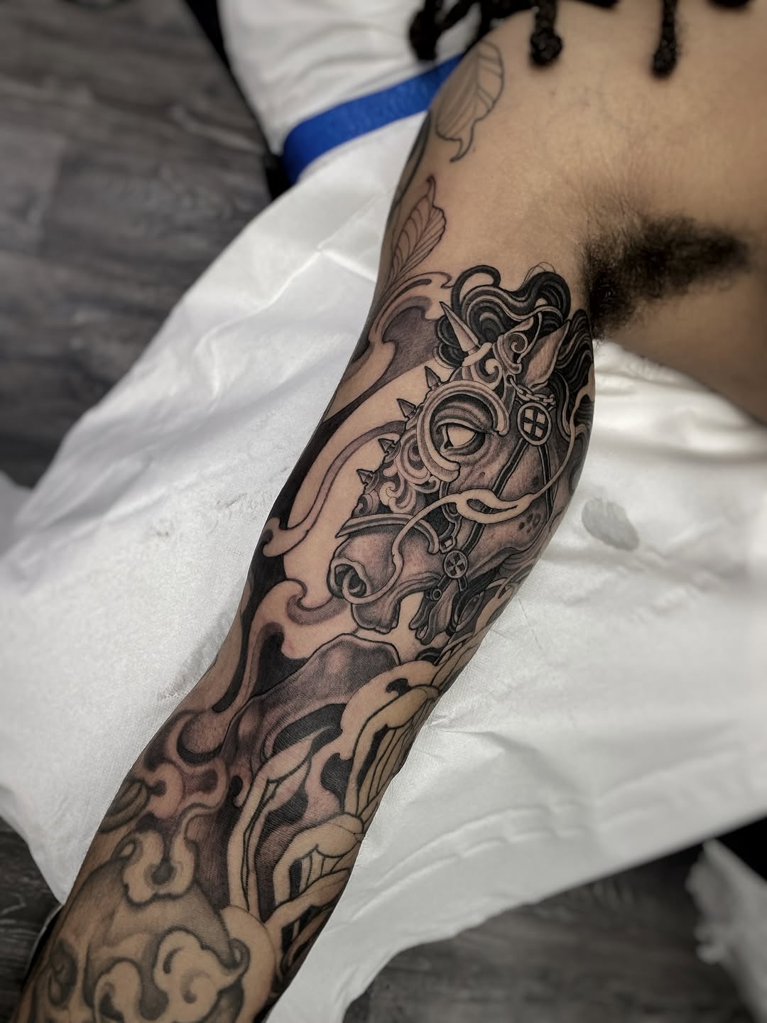 Black and grey ornamental tattoo with baroque flourishes and a central eye motif on the forearm.