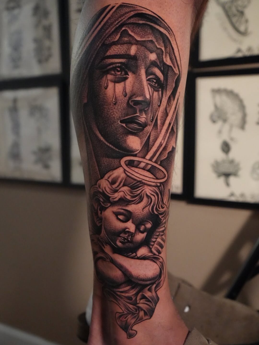 Black and grey portrait tattoo of a hooded weeping figure above a cherub on the forearm with detailed shading.