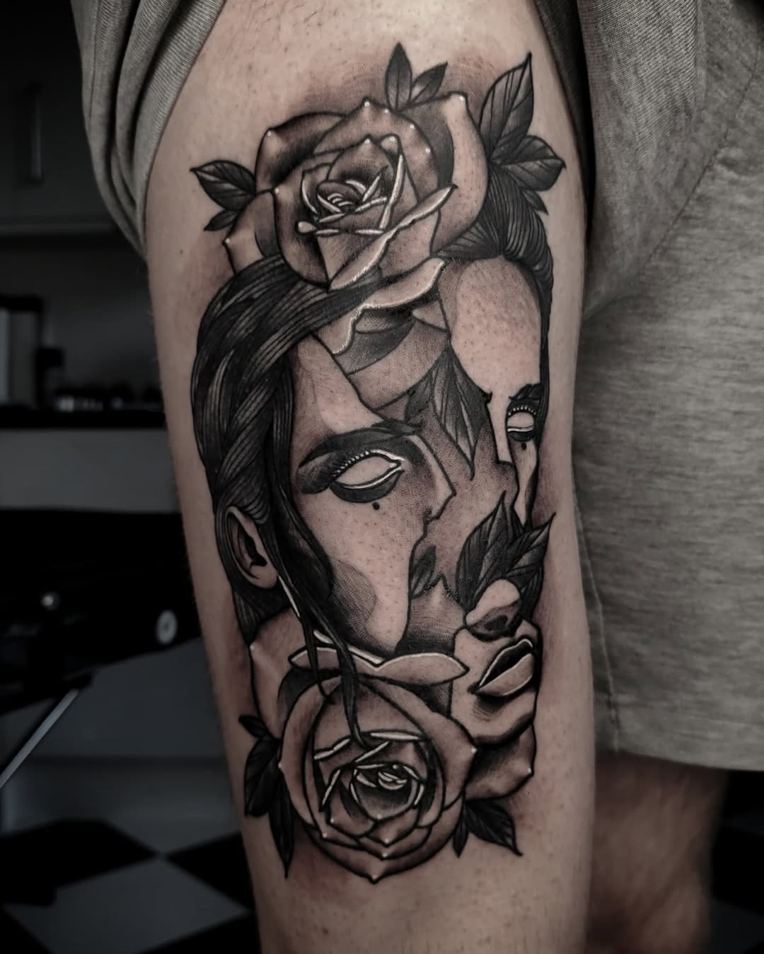 Black and grey portrait tattoo of a face with roses integrated into the design on the thigh.