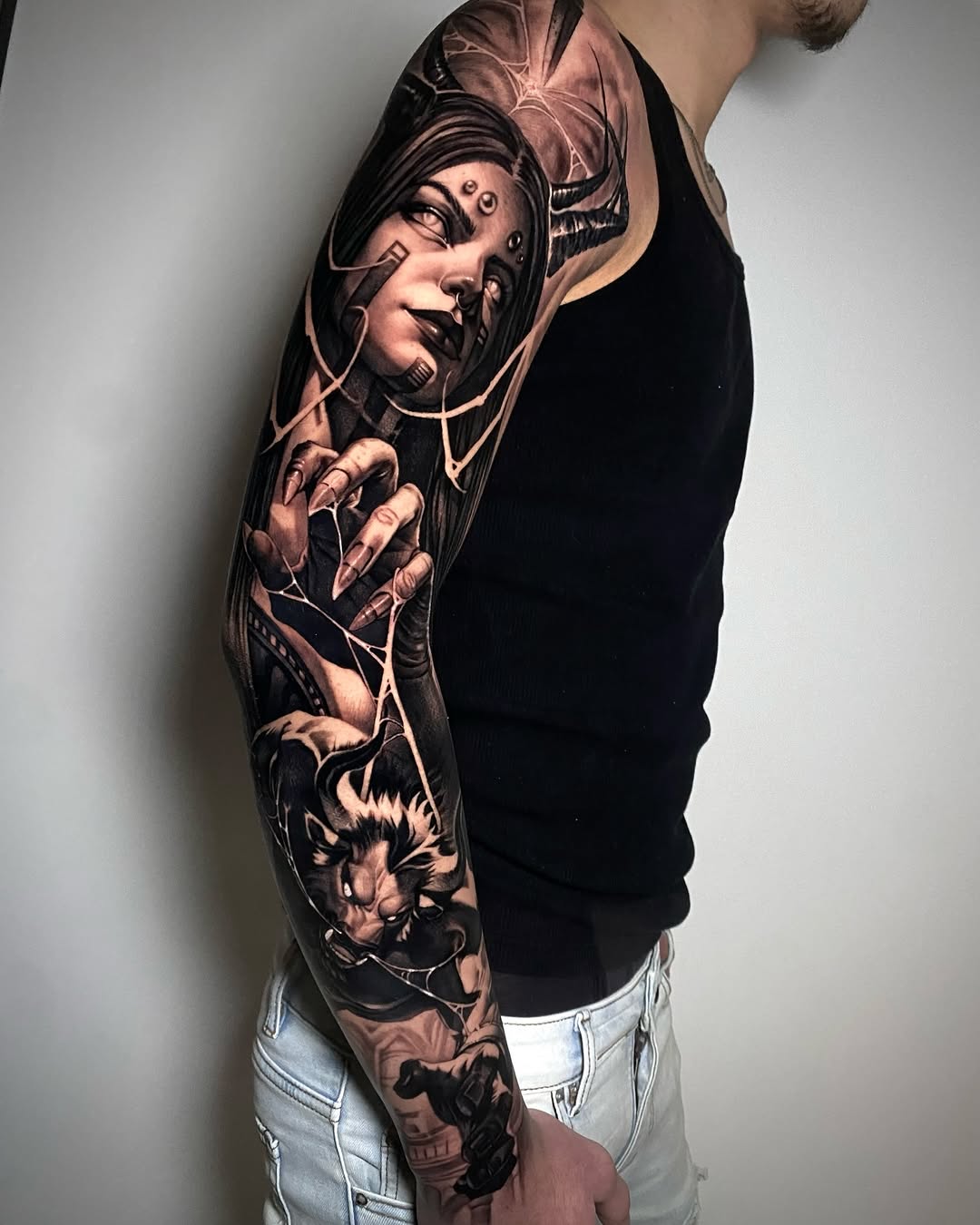 Black and grey sleeve tattoo featuring a portrait of a woman's face with flowing hair, decorative elements, and animals including a lion, covering the entire arm.
