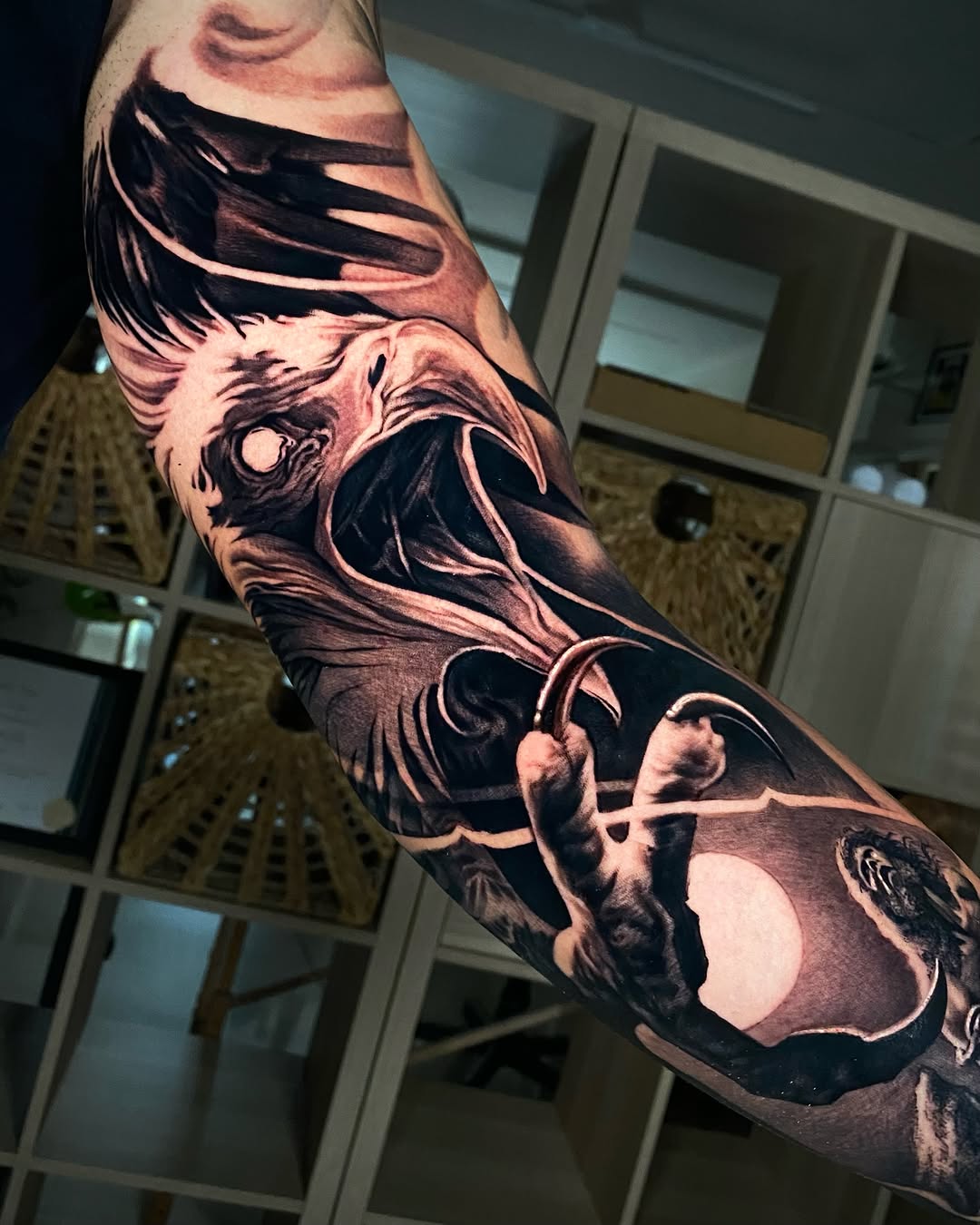 Black and grey realistic eagle head tattoo on forearm with detailed feathering and shading, featuring a crescent moon element.