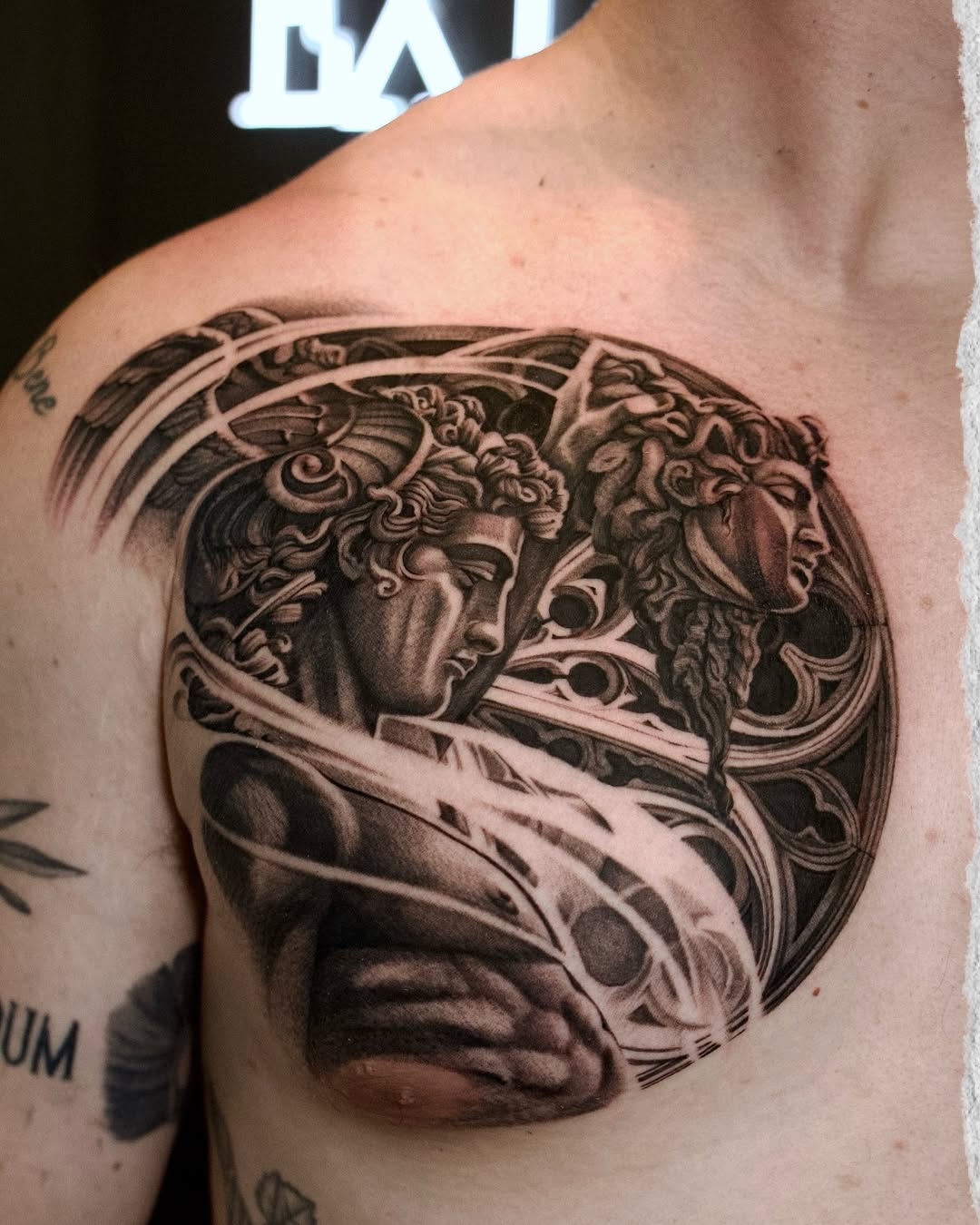 Black and grey portrait tattoo of two classical male heads with ornate decorative elements on upper chest.