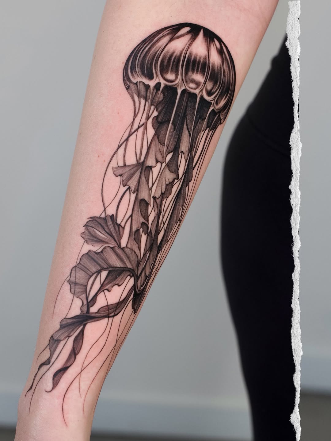 Black and grey jellyfish tattoo on forearm with detailed tentacles and flowing fins, rendered in realistic shading.