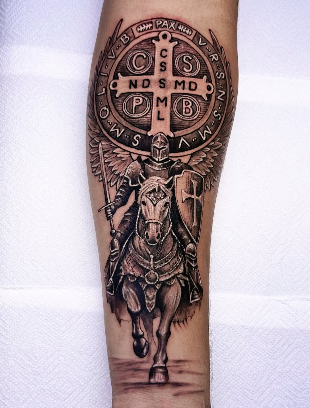 Armored knight on horseback wielding sword and shield beneath ornate circular medallion with cross and Latin text on calf.