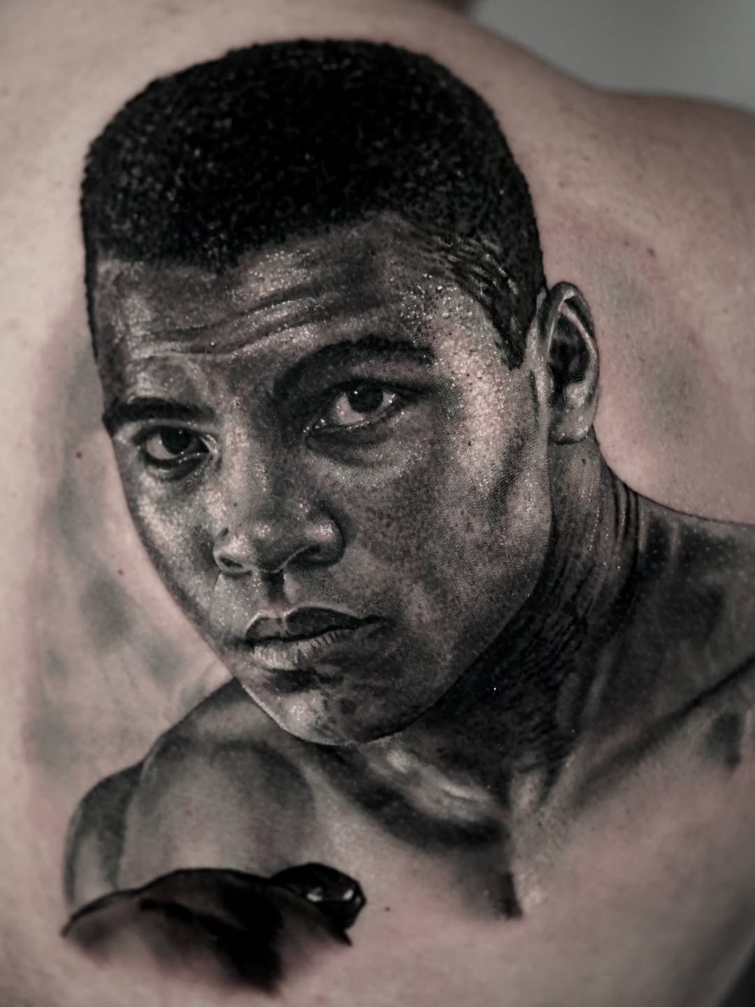 Black and grey portrait tattoo of a man's face with realistic tonal shading and smooth blending, placed on skin.